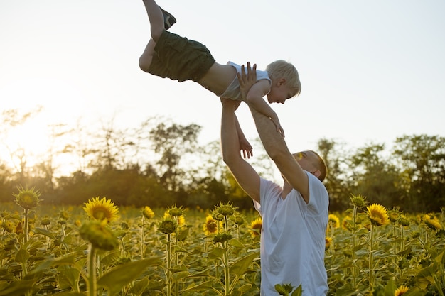 Vater wirft seinen kleinen Sohn auf dem Sonnenblumenfeld gegen den Himmel