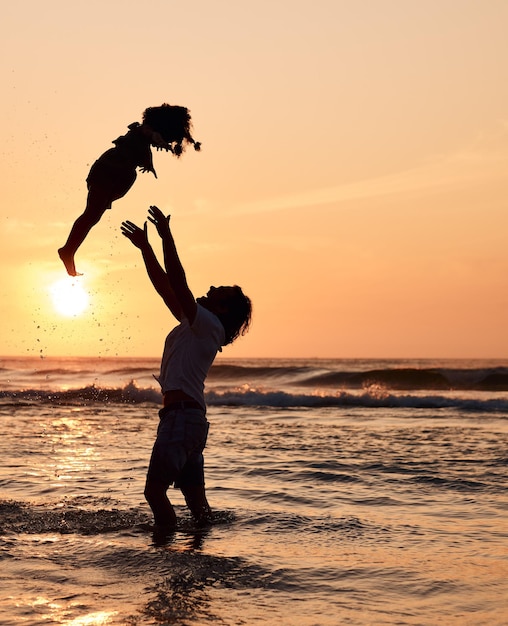 Vater wirft und Kind in die Luft bei Sonnenuntergang am Strand und Wellen im Meer für Glücksspaß und Unterstützung bei Abenteuern Elternkind und Silhouette von Papa im Meer mit Liebe, ein Spiel mit Mädchen zu spielen