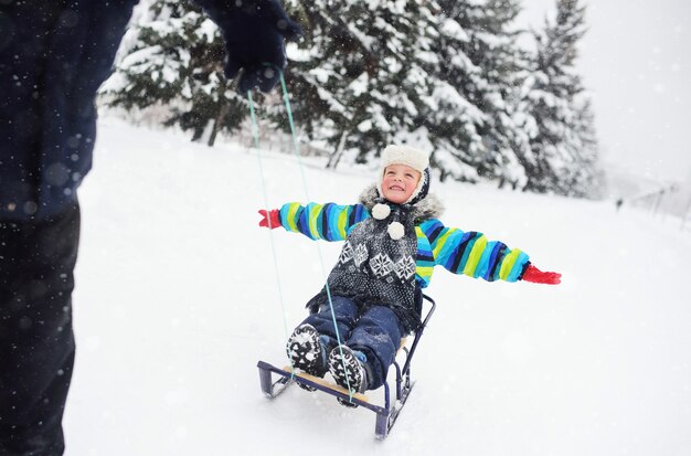 Vater zieht einen Seilschlitten, auf dem ein kleiner Sohn in einer gestreiften Winterjacke sitzt