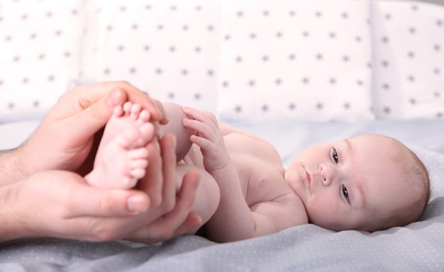 Vaterhände halten kleine Babyfüße auf Bett