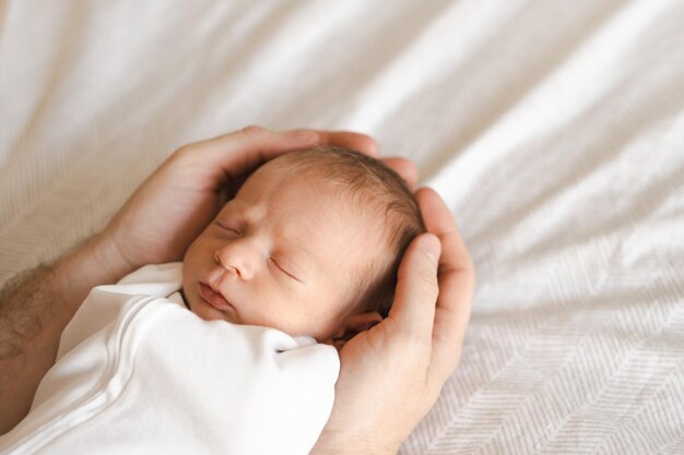 Vaterjunger Mann, der kaukasischen haarigen Brunet niedliches Neugeborenes hält, das ein oder zwei Wochen Kind auf dem Bett in männlichen Händen drinnen schläftPflegeliebe-Glück-Konzept Kopieren Sie Platz für Text
