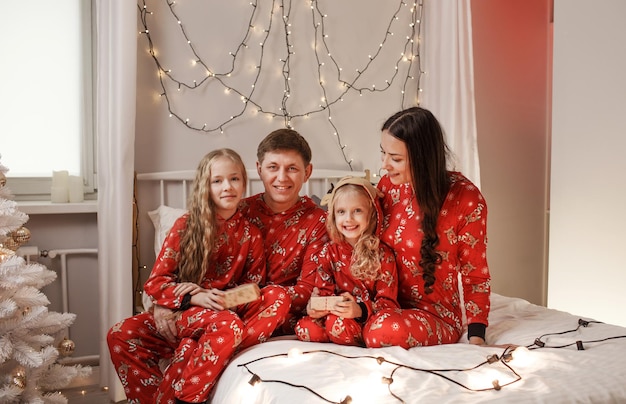 Vatermutter und zwei kleine Töchter im Bett Glückliche Familie im roten Weihnachtspyjama im Schlafzimmer am Weihnachtsmorgen. Neujahr