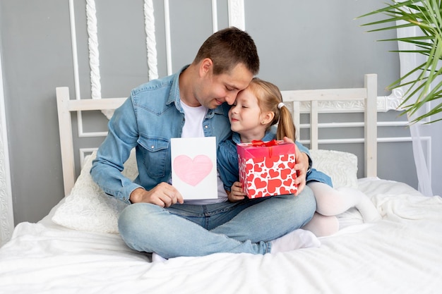 Vatertagskonzept eine Mädchentochter gibt ihrem geliebten Vater ein Geschenk und eine Herzkarte das Konzept der glücklichen Vaterschaft und eines Urlaubs