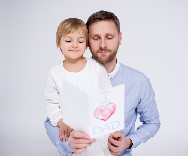 Vatertagskonzept - kleines Mädchen, das ihrem Vater handgemachte Grußkarte auf weißem Hintergrund gibt