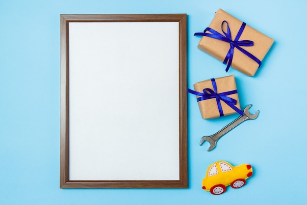 Vatertagskonzeptkarte mit dem Arbeitswerkzeug des Mannes auf den blauen Hintergrund- und Geschenkkästen eingewickelt im Kraftpapier und mit blauem Bogen gebunden.