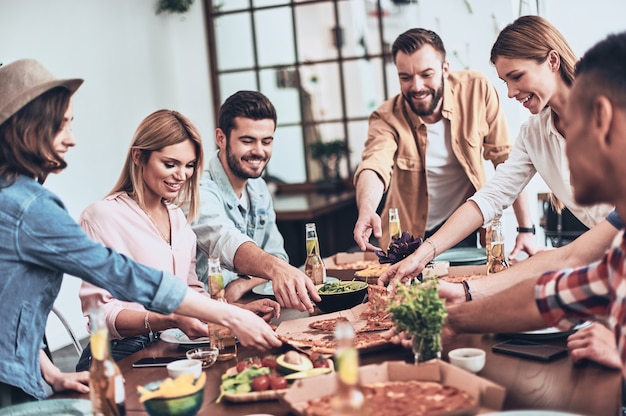 Se ve delicioso. Grupo de jóvenes en ropa casual recogiendo pizza y sonriendo