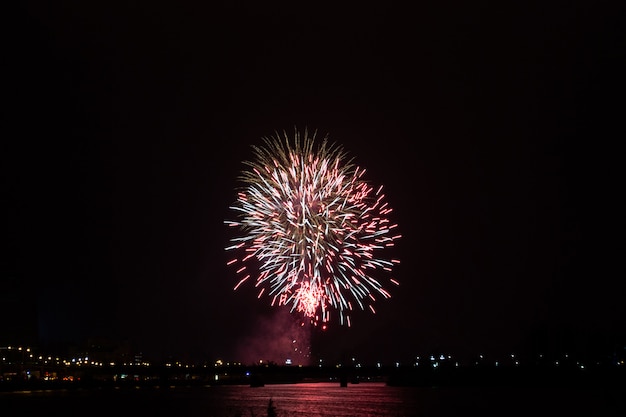 Ve a los fuegos artificiales en el fondo oscuro de la noche sobre la ciudad. Concepto de vacaciones y diversión