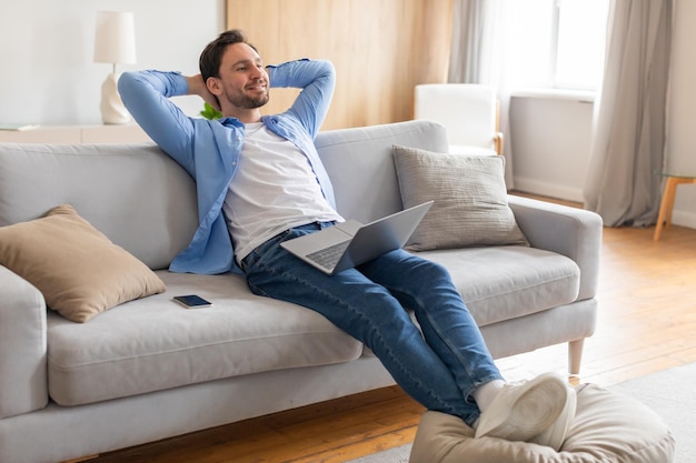 Se ve a un hombre de mediana edad relajándose en un cómodo sofá absorto en la pantalla de su portátil.