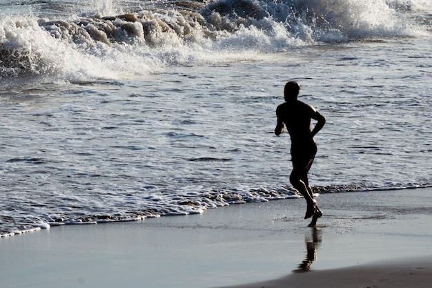 Se ve a un hombre en silueta corriendo por la playa a última hora de la tarde en la ciudad de Salvador Bahia