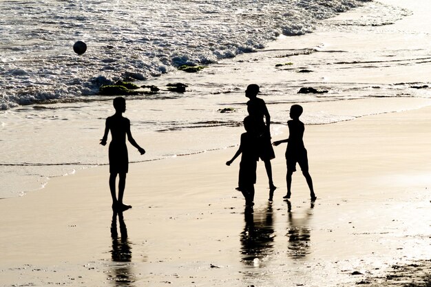 Se ve a jóvenes en silueta jugando al fútbol de playa a última hora de la tarde en la ciudad de Salvador Bahia