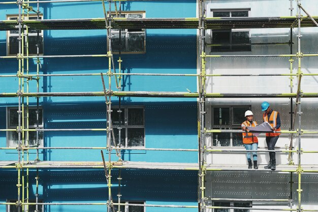 Vea a los expertos en acción Captura de un hombre y una mujer jóvenes repasando los planos de construcción en un sitio de construcción