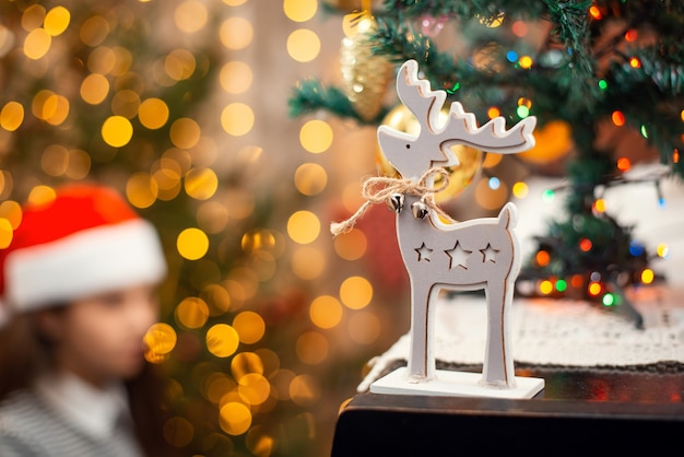 Veado de madeira como símbolo de Natal em pé no piano, atmosfera dos feriados. Luzes brilhantes, decoração festiva e pianista feminina no fundo.