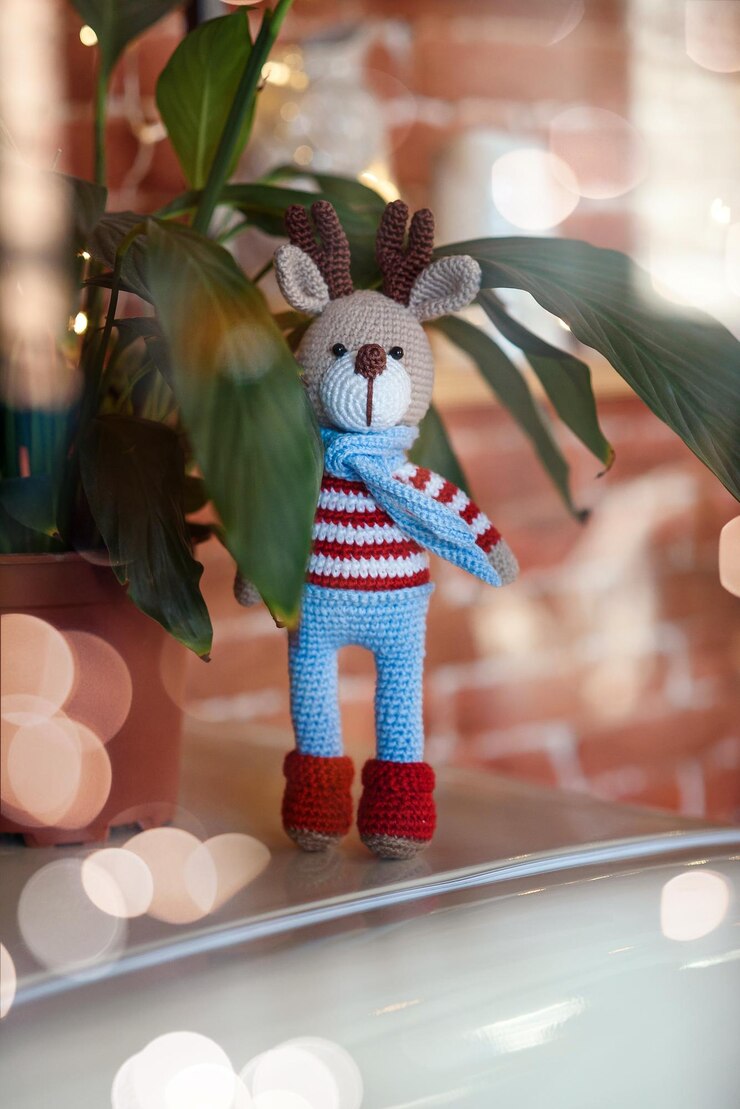 Veado de Natal fechado brinquedo amigurumi veado em suéter listrado e elegante lenço azul está perto