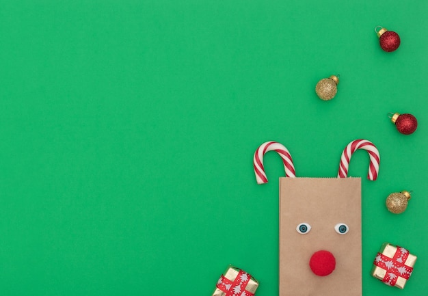 Veado de Natal feito de sacola artesanal e duas bengalas de Natal com caixas de presente e bolas de Natal em fundo verde