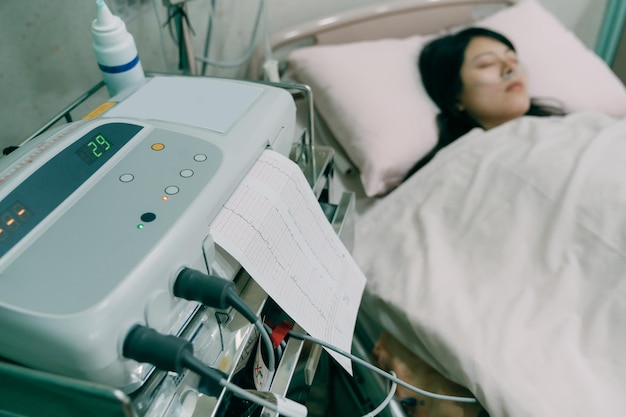El vector del ventilador médico colocado junto a la cama con papel impreso sale del resultado de la respiración del paciente. vista borrosa de una joven enferma asiática que duerme en la habitación del hospital con un tubo nasal que ayuda a respirar.