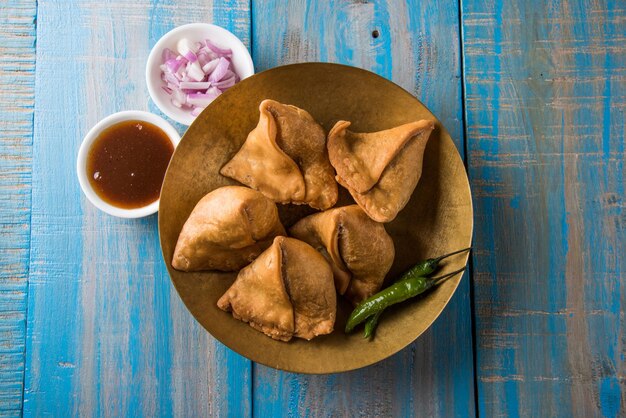 Veg Samosa - é um lanche da hora do chá em forma de triângulo indiano crocante e picante servido com pimenta verde frita, cebola e chutney ou ketchup