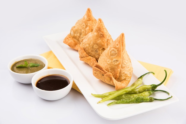 Veg Samosa es un bocadillo o comida chatarra popular en la India que se sirve con frijoles verdes fritos, cebolla y salsa picante o salsa de tomate