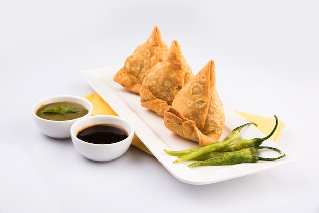 Veg Samosa ist ein in Indien beliebter Snack oder Junk Food, serviert mit gebratenem grünem Chili, Zwiebeln und Chutney oder Ketchup