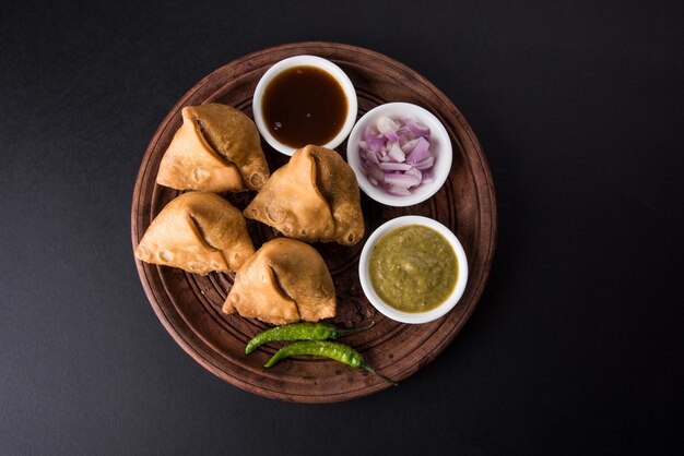 Foto veg samosa - ist ein knuspriger und würziger indischer tea time snack in dreiecksform, serviert mit gebratenem grünem chili, zwiebeln & chutney oder ketchup