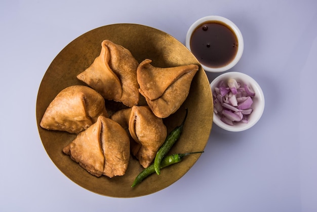 Veg Samosa - ist ein knuspriger und würziger indischer Tea Time Snack in Dreiecksform, serviert mit gebratenem grünem Chili, Zwiebeln & Chutney oder Ketchup