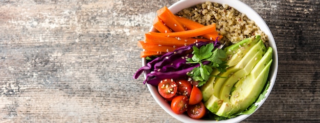 Vegan Buddha Bowl con verduras crudas frescas y quinua en vista panorámica de mesa de madera