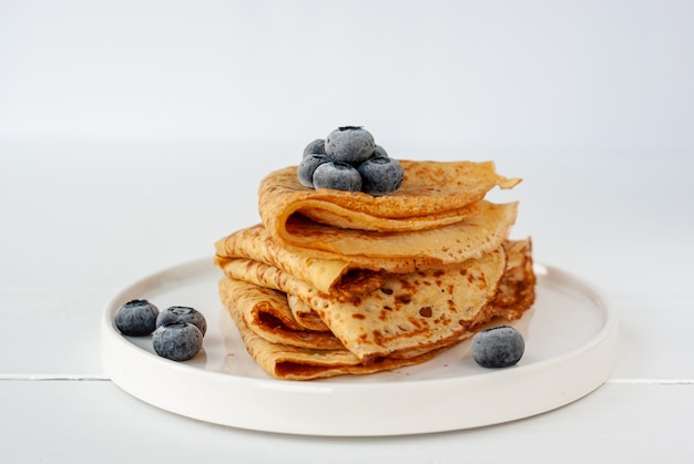 Vegane Crepes aus Kichererbsenmehl, glutenfreiem Allzweckmehl und Hafermilch mit gefrorenen Blaubeeren auf einem weißen Holztisch