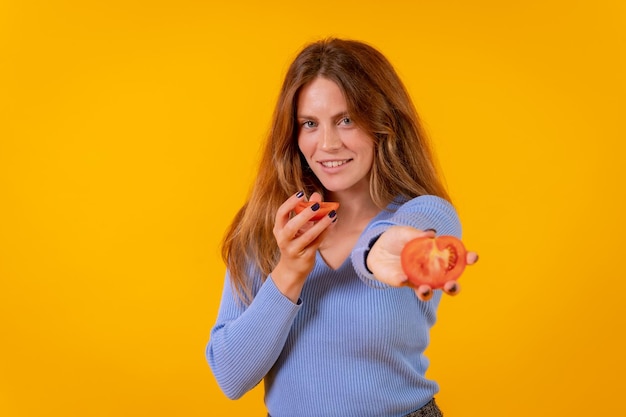 Vegane Frau lächelt und hält eine geschnittene Tomate auf gelbem Hintergrund