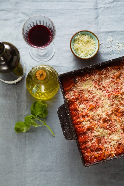 Vegane Lasagne mit Linsen und Erbsen in einem Backblech auf einem Tisch mit einer blauen Leinentischdecke. und Rotwein in Gläsern