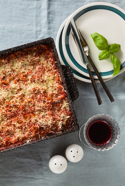 Vegane Lasagne mit Linsen und Erbsen in einem Backblech auf einem Tisch mit einer blauen Leinentischdecke. und Rotwein in Gläsern