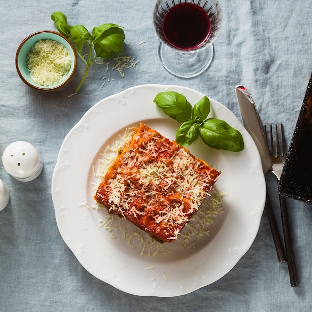 Vegane Lasagne mit Linsen und Erbsen in einem Backblech auf einem Tisch mit einer blauen Leinentischdecke. und Rotwein in Gläsern