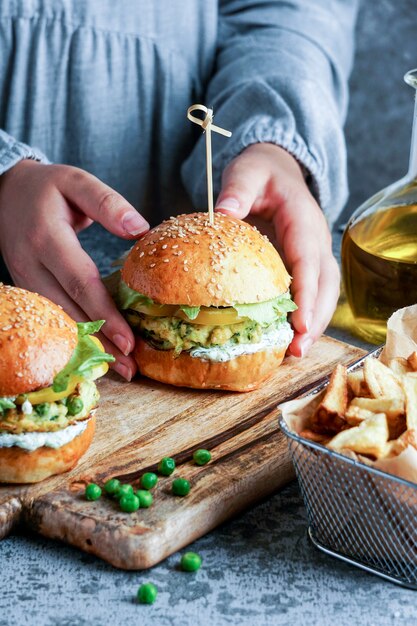 Vegane Linsenburger in den Händen der Frauen, mit Salat und Joghurtsauce auf weißem Hintergrund. Lebensmittelkonzept auf pflanzlicher Basis.