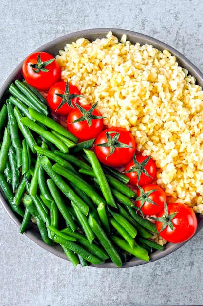 Vegane Schüssel mit Bulgur, Kirschtomaten und grünen Bohnen. Gesundes Essen in einer Schüssel. Vegane Lunch Bowl.