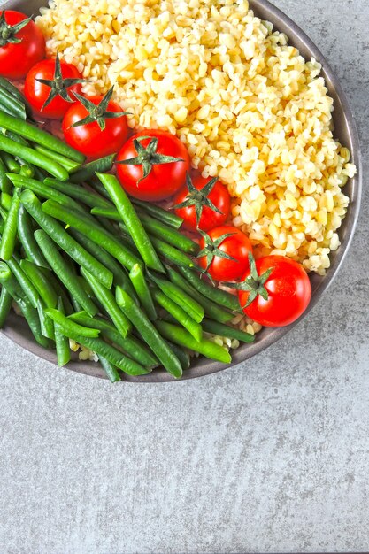 Vegane Schüssel mit Bulgur, Kirschtomaten und grünen Bohnen. Gesundes Essen in einer Schüssel. Vegane Lunch Bowl.