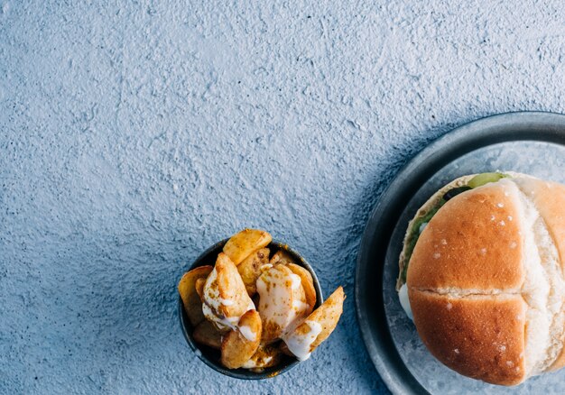 Veganer Burger mit Pommes Frites mit Gewürzen und Soße in einer Metallschale auf blauem Tischhintergrund