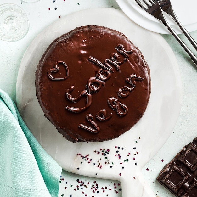 Veganer festlicher Schokoladen-Sacher-Kuchen mit Aprikosenmarmelade auf dem Tisch, geschrieben von Schokolade