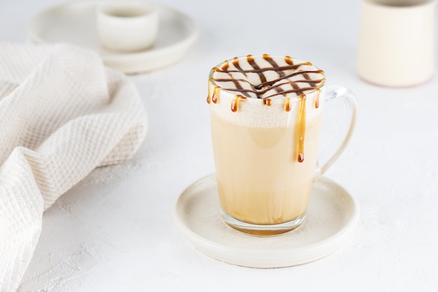 Veganer Karamell-Macchiato-Kaffee mit Kokoscreme in einem Glasbecher auf einem Leuchttisch.