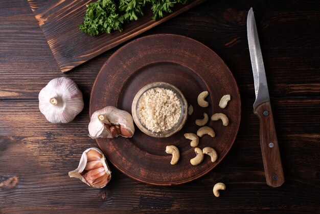 Veganer Parmesan-Käse-Cashew-Nuss mit Petersilie und Knoblauchzehen auf Holzhintergrund, veganes Essen, Nahaufnahme.