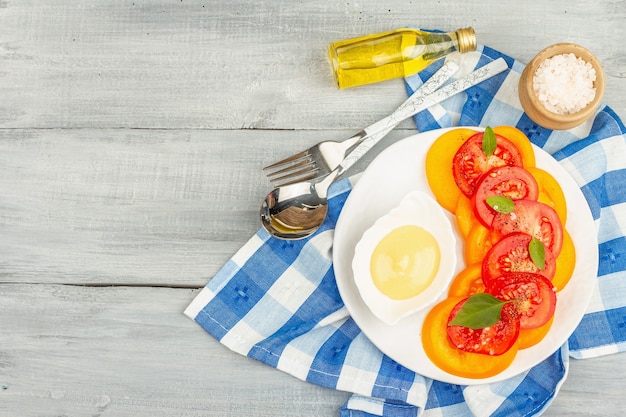 Veganer Tomatensalat mit frischen Basilikumblättern, Gewürzen und leckerer Sauce. Rotes und oranges Gemüse, Tischdekoration. Holzhintergrund, Ansicht von oben