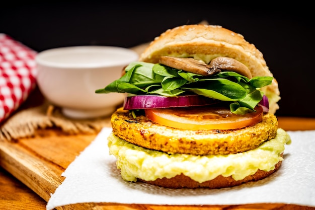 Veganer Veggie-Protein-Burger mit Tomaten-Rucola, roten Zwiebeln, Pilzen und Avocado-Mayonnaise auf einem Holzbrett und schwarzem Hintergrund Gehackte Ansicht Text kopieren