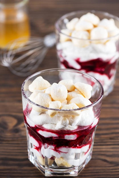 Veganes Dessert mit Aquafaba Baiser Kokoscreme und Kirschen im Glas auf einem Holztisch