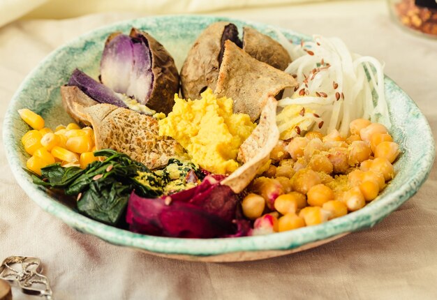 Veganes Detox-Mittagessen mit einer lila Kartoffel, gedünstetem Spinat und Hummus mit Maiscrackern.