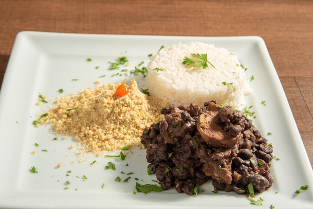 Veganes Essen veganer Feijoada-Reis und Farofa auf einem weißen Teller über Holz selektiver Fokus