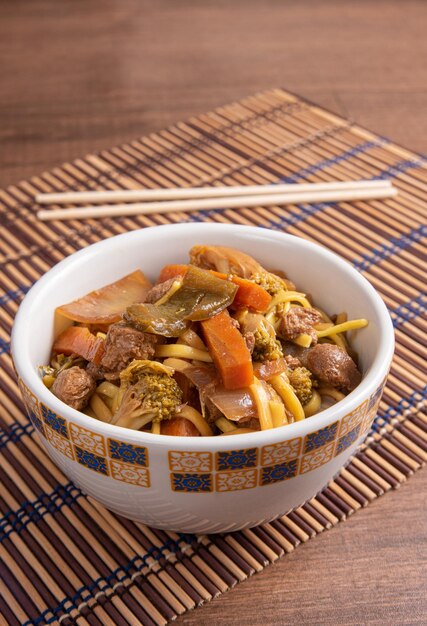 Veganes Essen Veganes Yakisoba mit Essstäbchen in einer Schüssel auf Bambusmatte über Holz selektiver Fokus