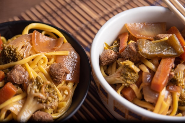 Veganes Essen Veganes Yakisoba mit Essstäbchen in einer Schüssel auf Bambusmatte über Holz selektiver Fokus