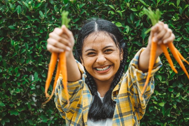 Veganes Gemüse essen für gesundes, gut fürs Leben Konzept Junge Teenager-Hand, die ein glückliches Lächeln der Babykarotte hält