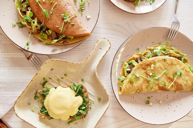 Veganes gesundes Frühstück Eier Benedikt mit pflanzlicher Soße Sauerteigbrot Tofu junges Zwiebelgemüse Pfannkuchen gefüllt mit Pilzen Erbsensprossen Avocado