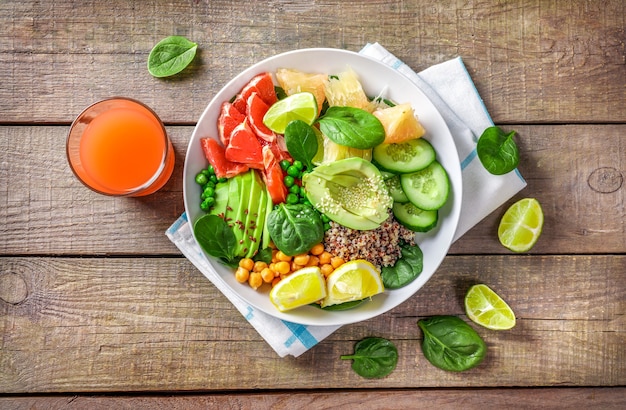 Foto veganes lebensmittelkonzept: quinoa mit avocado, gurken, grünen erbsen, kichererbsen, spinat und zitrusfrüchten auf holzhintergrund.