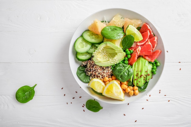 Veganes Lebensmittelkonzept: Quinoa mit Avocado, Gurken, grünen Erbsen, Kichererbsen, Spinat und Zitrusfrüchten auf weißem Hintergrund. Ansicht von oben.