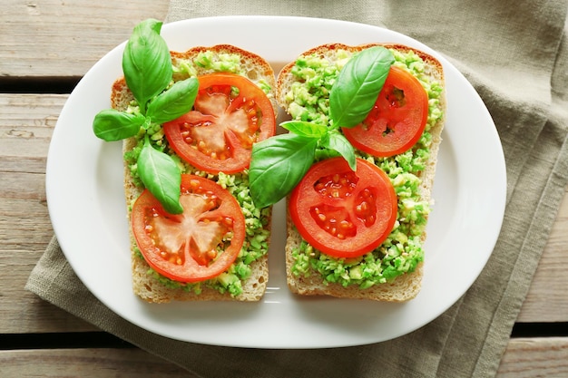 Veganes Sandwich mit Avocado und Gemüse auf Teller auf Holzhintergrund