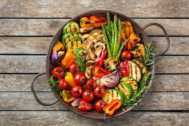 Foto veganes, vegetarisches, saisonales, sommerliches essenskonzept. gegrilltes gemüse in einer pfanne auf einem holztisch. draufsicht flach legen hintergrund